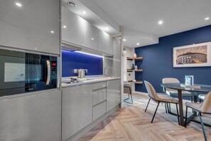 A modern kitchen with a built-in microwave, a blue-lit island, and a dining area with a table and chairs. - Roomzzz Leeds City (Leeds)