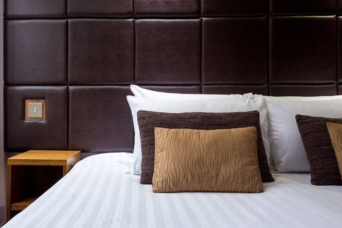 A hotel room with a large bed, a wooden nightstand, and a dark headboard.
