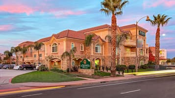 Un hôtel dont l’enseigne indique « La Quinta Inn & Suites », avec une façade en pierre, de nombreux balcons et des palmiers.