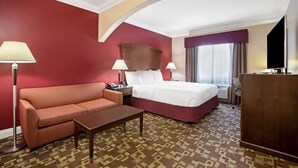 A hotel room with a red wall, a bed, a sofa, a desk, and a lamp. - La Quinta Inn & Suites by Wyndham Moreno Valley (Moreno Valley)
