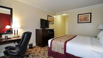 A hotel room with a bed, desk, chair, TV, and a trash bin.