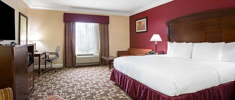 A hotel room with a large bed, a desk with a chair, a television, and a window with curtains.