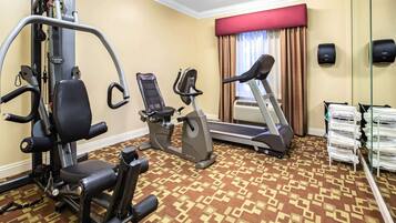 Habitación de hotel con zona de fitness que incluye una máquina de pesas, una elíptica y una cinta de correr.