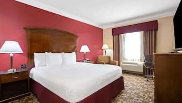 Ein Hotelzimmer mit einem großen Bett, zwei Nachttischen inklusive Lampen, einem Sessel, einem Schreibtisch und einem großen Fenster mit Vorhängen.