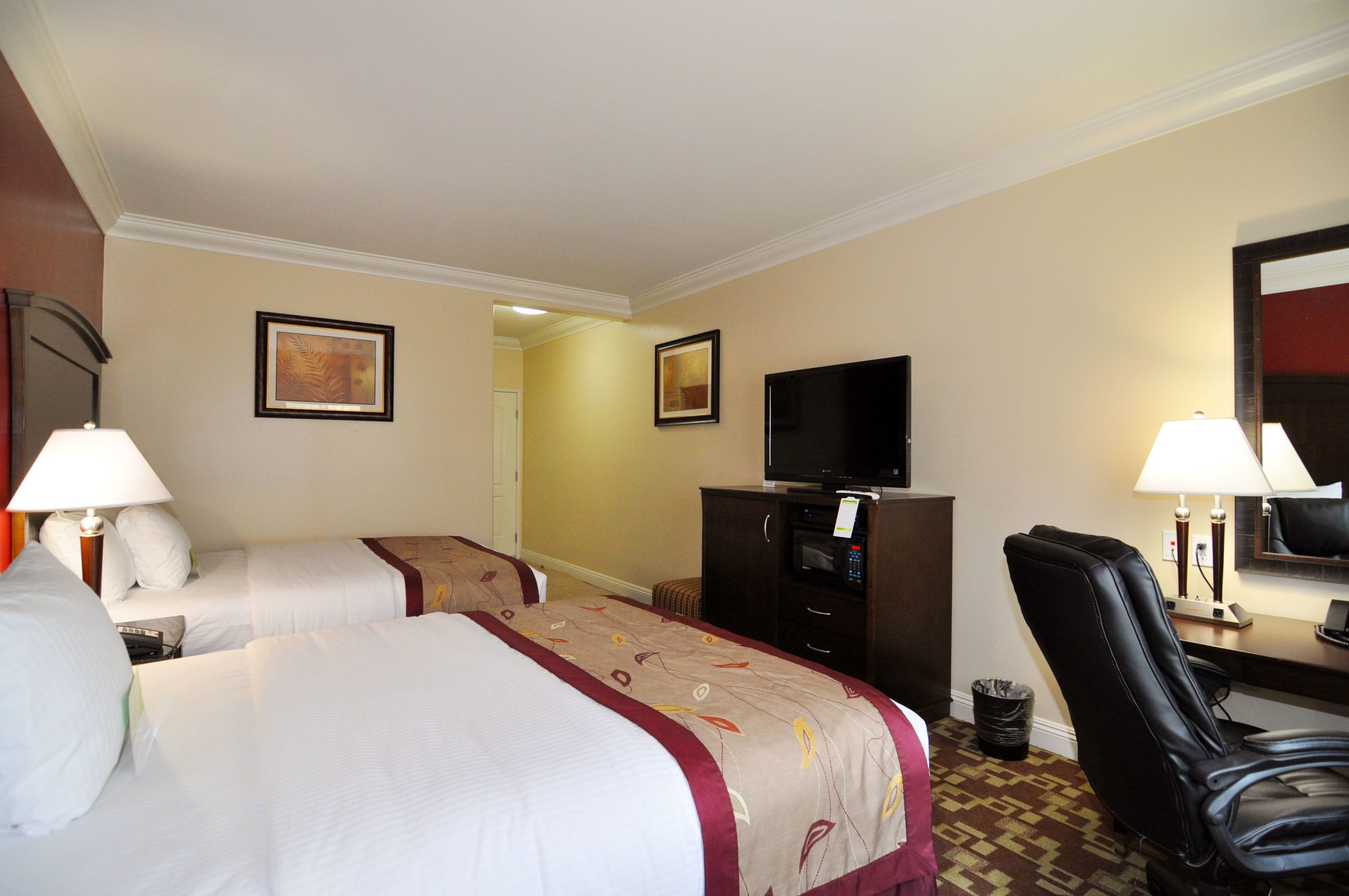 A hotel room with two beds, a TV, a desk with a lamp, and a chair.