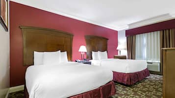 Une chambre d’hôtel avec deux lits, une grande tête de lit en bois, une moquette à motifs et une fenêtre avec des rideaux.