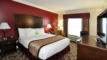 A hotel room with a large bed, two bedside lamps, a desk with a TV, and a window with curtains.