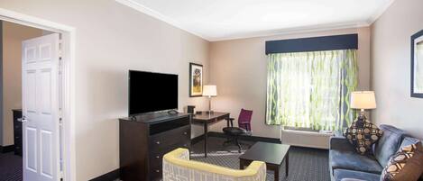 A hotel room with a flat-screen TV, a desk, a sofa, and a chair.