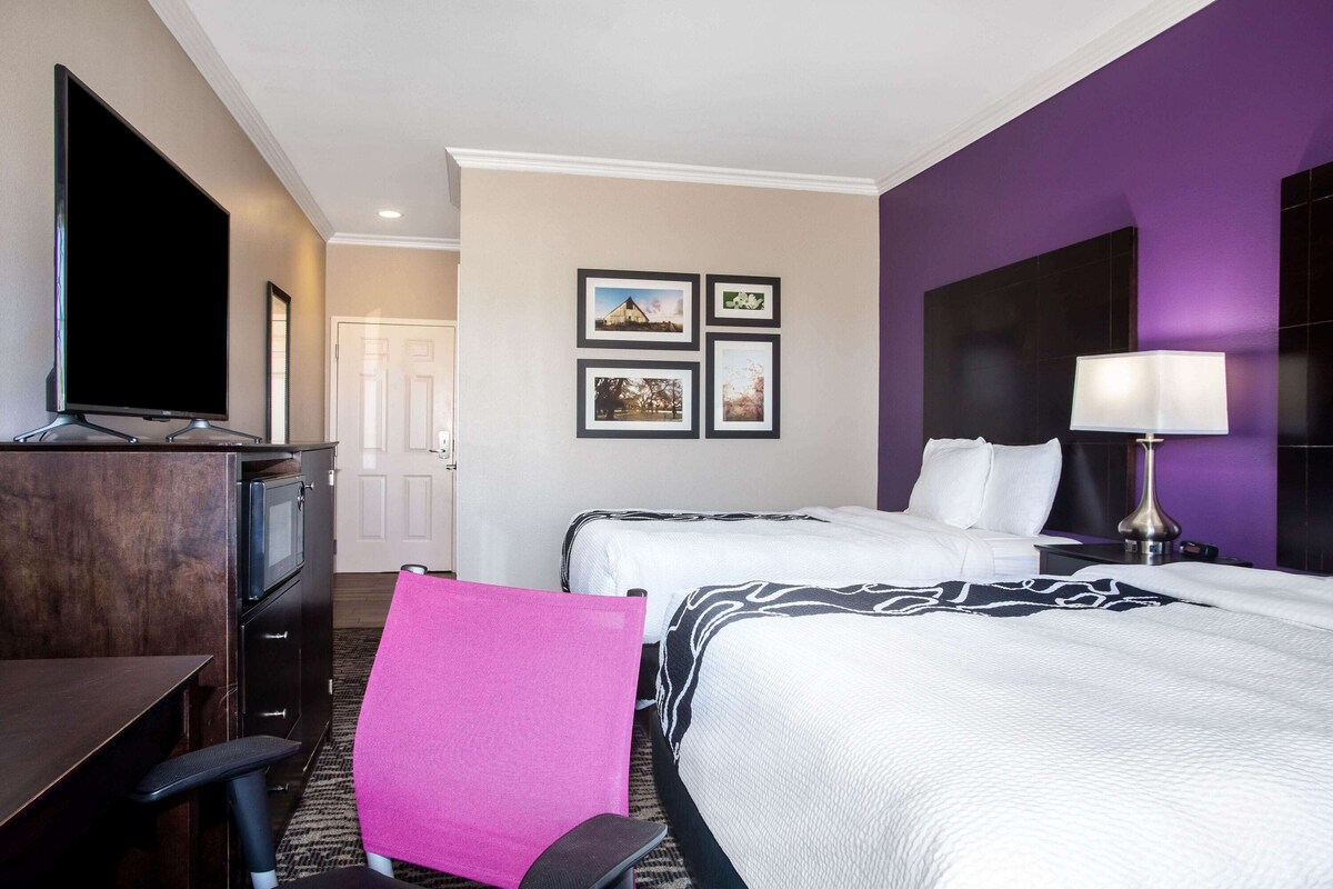 A hotel room with two beds, a desk with a TV, a chair, and framed pictures on the wall.