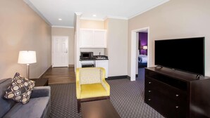 A hotel room with a sofa, a yellow armchair, a TV, a lamp, and a kitchenette in the background. - La Quinta Inn & Suites by Wyndham Columbus TX (Columbus)