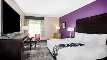 Habitación de hotel con una cama grande, un escritorio con televisor de pantalla plana, una silla, una lámpara y una ventana con cortinas.