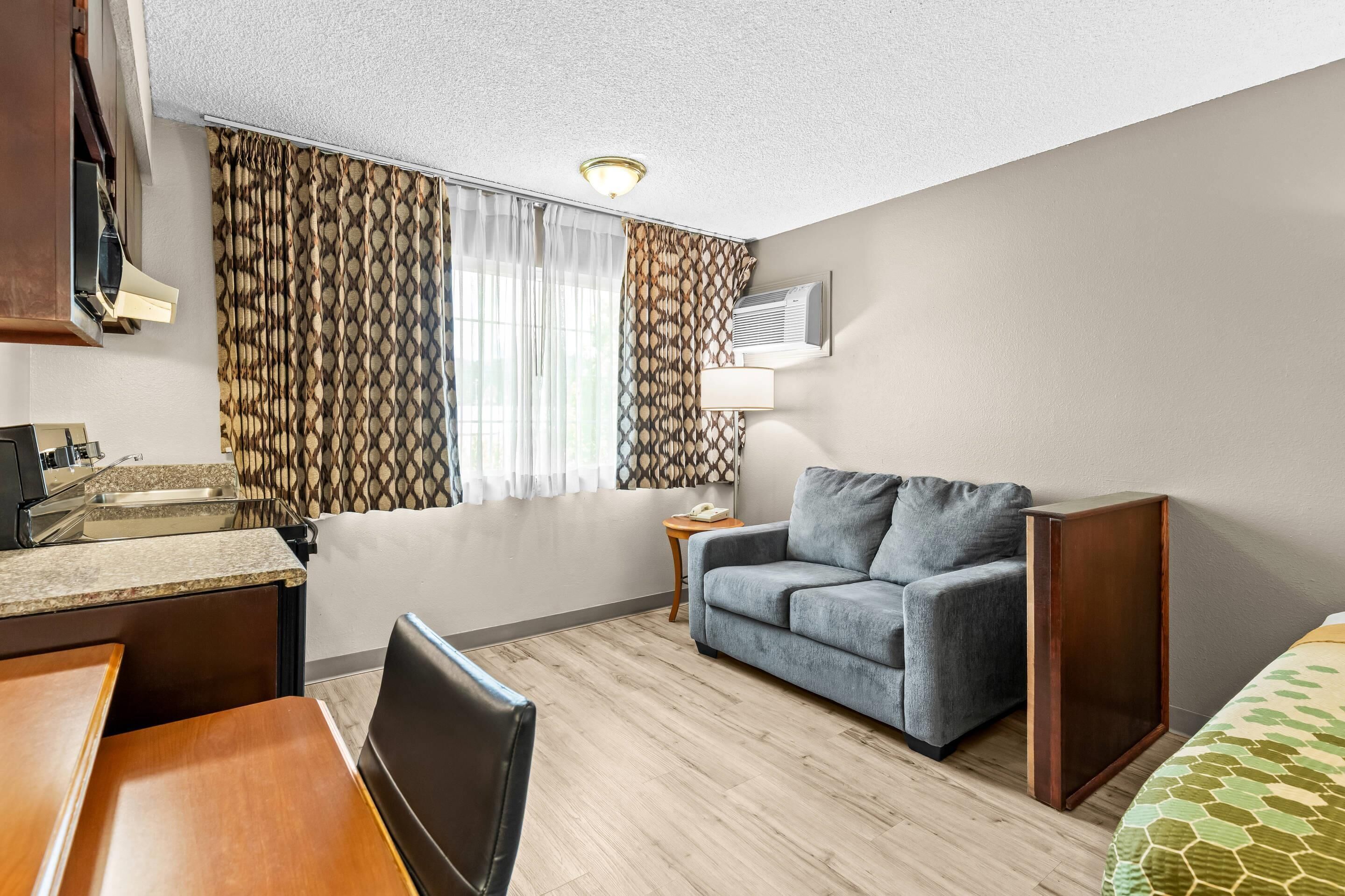 Una habitación de hotel compacta con kitchenette, un sofá, una mesita y una cama.