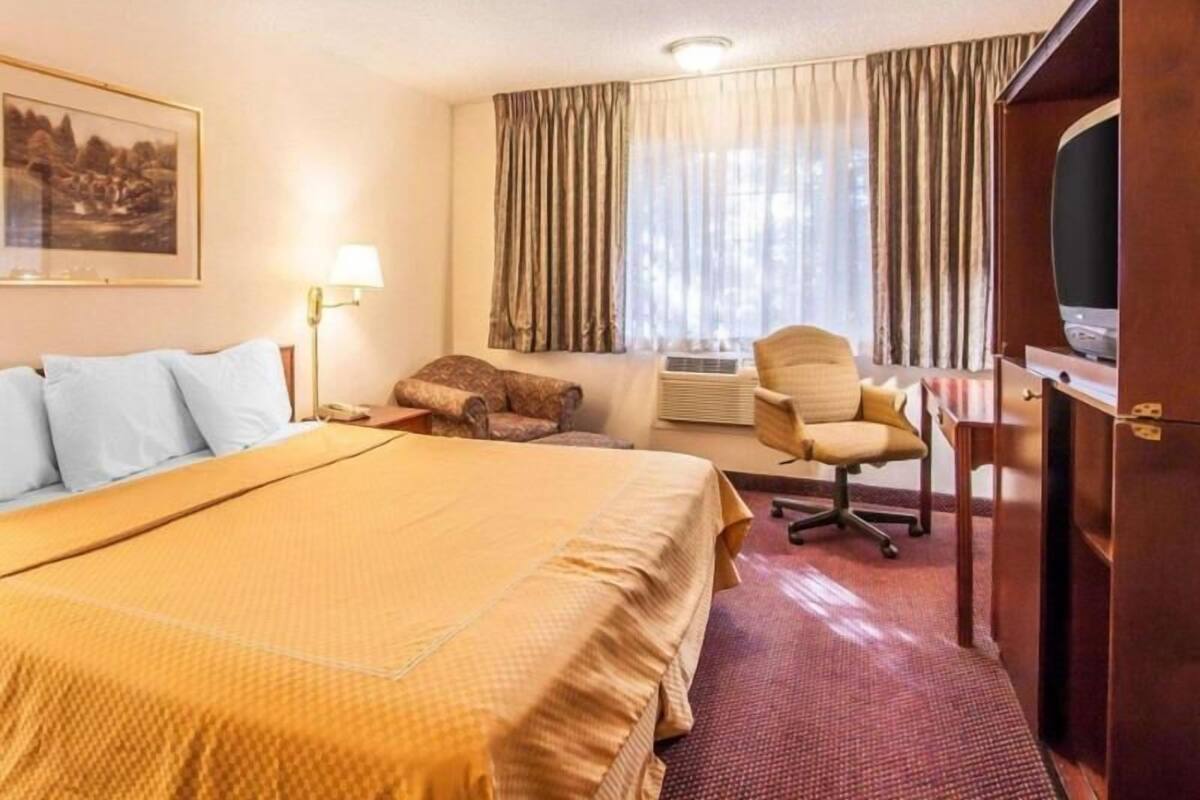 A hotel room with a large bed, a desk with a chair, a television, and a window with curtains.