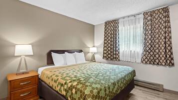 A hotel room with a bed, nightstands, lamps, a window with curtains, and a wall-mounted heater.