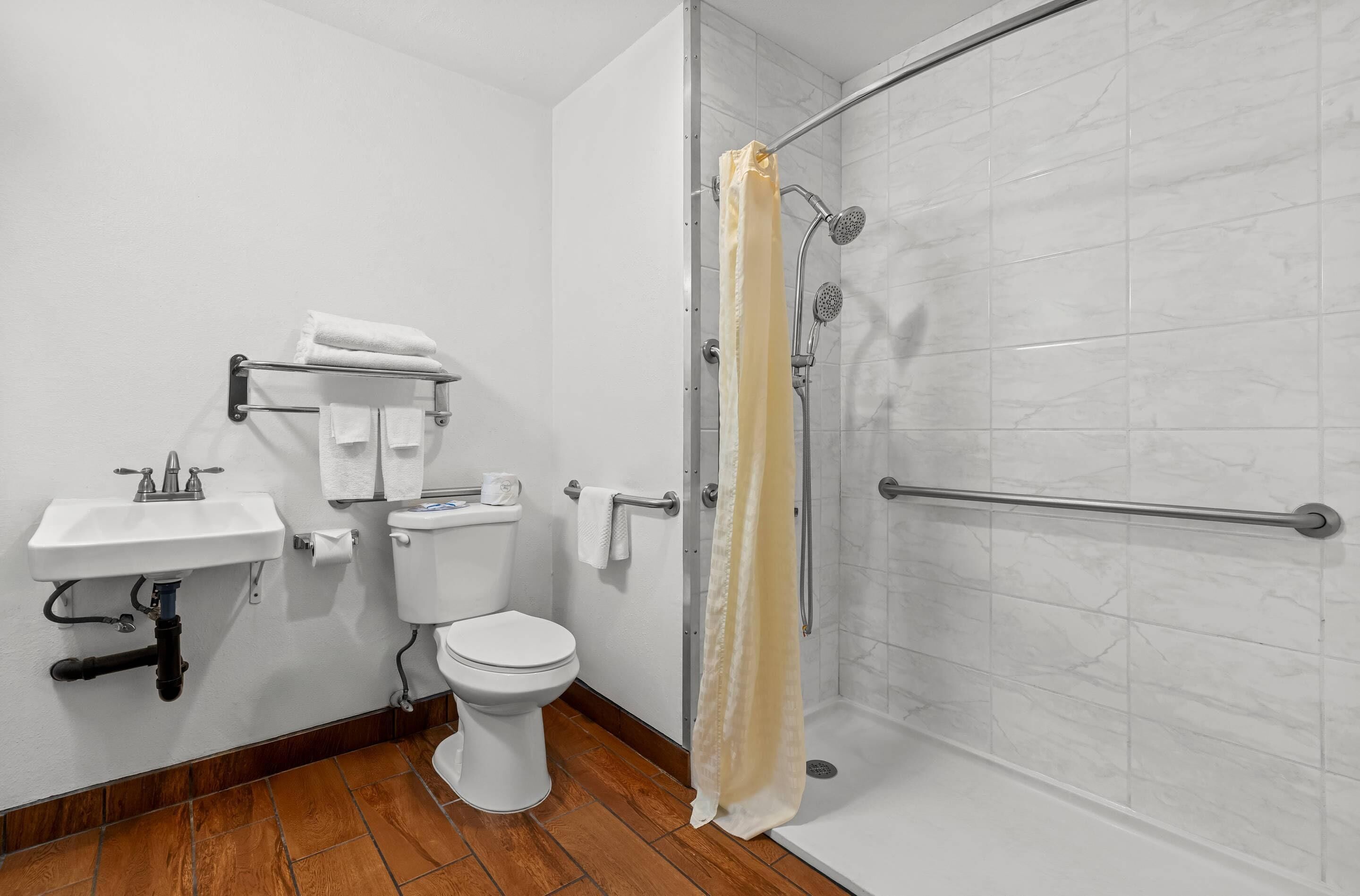 A bathroom with a toilet, sink, shower, and a towel rack.