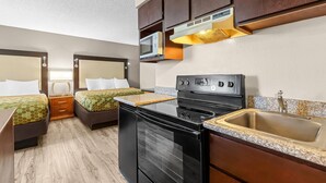 A compact kitchen with a stove, microwave, and sink. There are two beds with matching headboards and a small bedside table with drawers. - Rodeway Inn & Suites Portland West - Beaverton (Portland)
