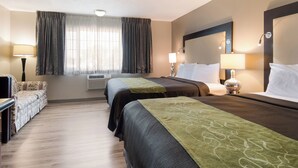 A hotel room with two beds, a sofa, a TV, and a large window with curtains. - Rodeway Inn & Suites Portland West - Beaverton (Portland)