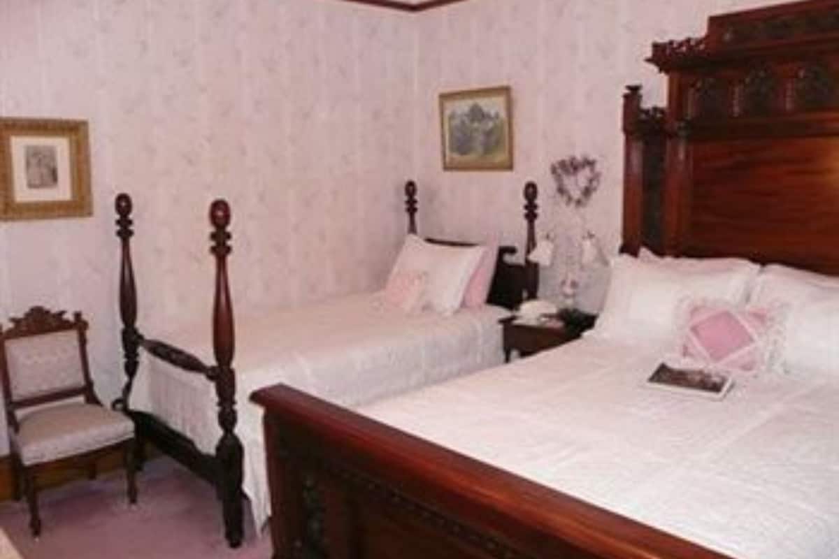Une chambre avec deux lits simples, une tête de lit en bois, une table de chevet, une chaise et un tableau encadré au mur.