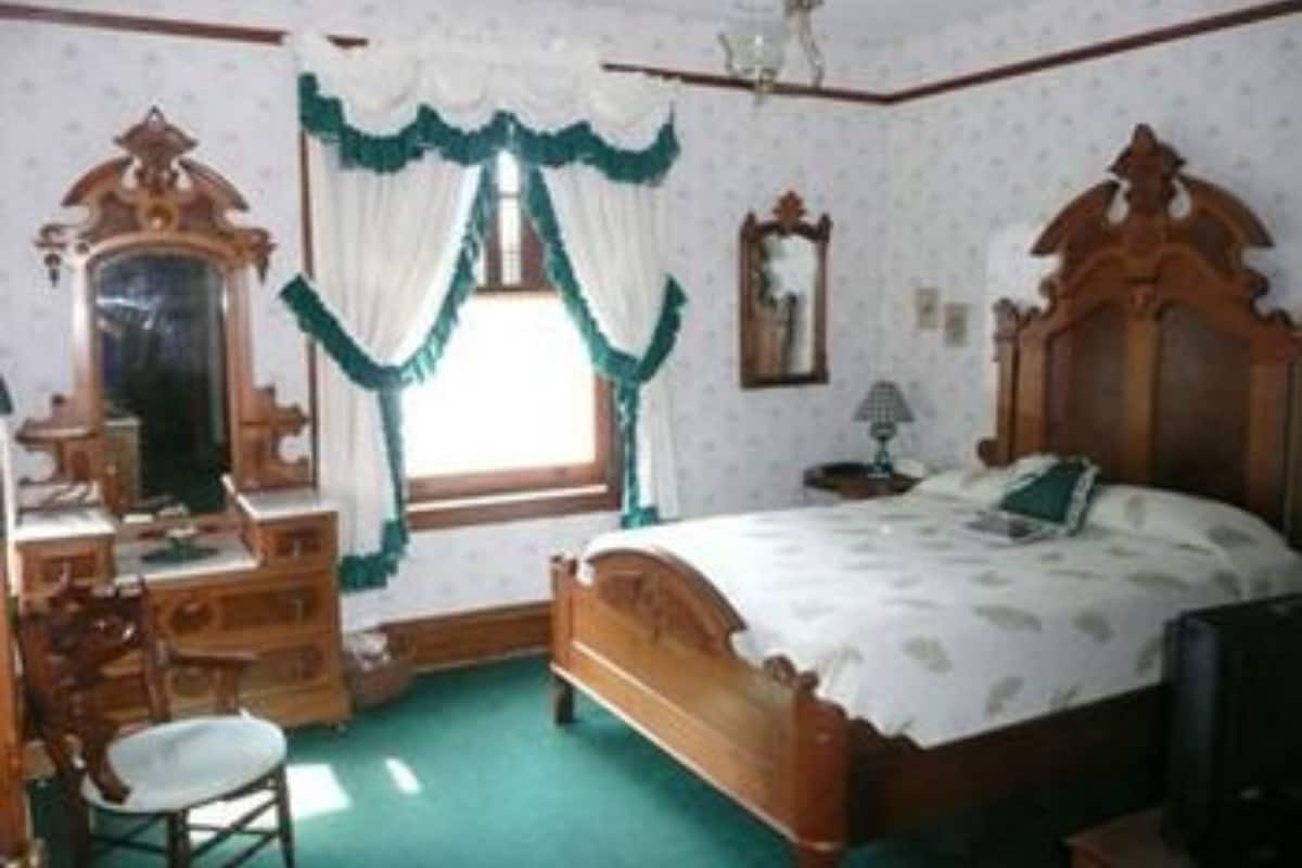 Une chambre à coucher de style traditionnel, avec un lit en bois, une commode, un miroir et une fenêtre avec des rideaux.