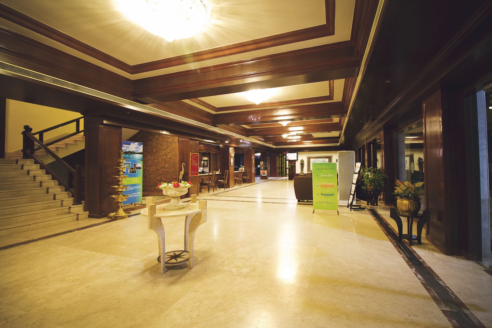 A hotel lobby with a marble floor, wooden paneling, a reception desk, and a staircase.