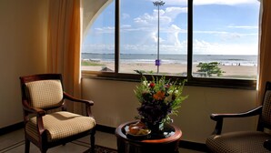 A room with a large arched window overlooking a beach, two armchairs, and a small table with a vase of flowers. - Paradise Isle Beach Resort (Udupi)