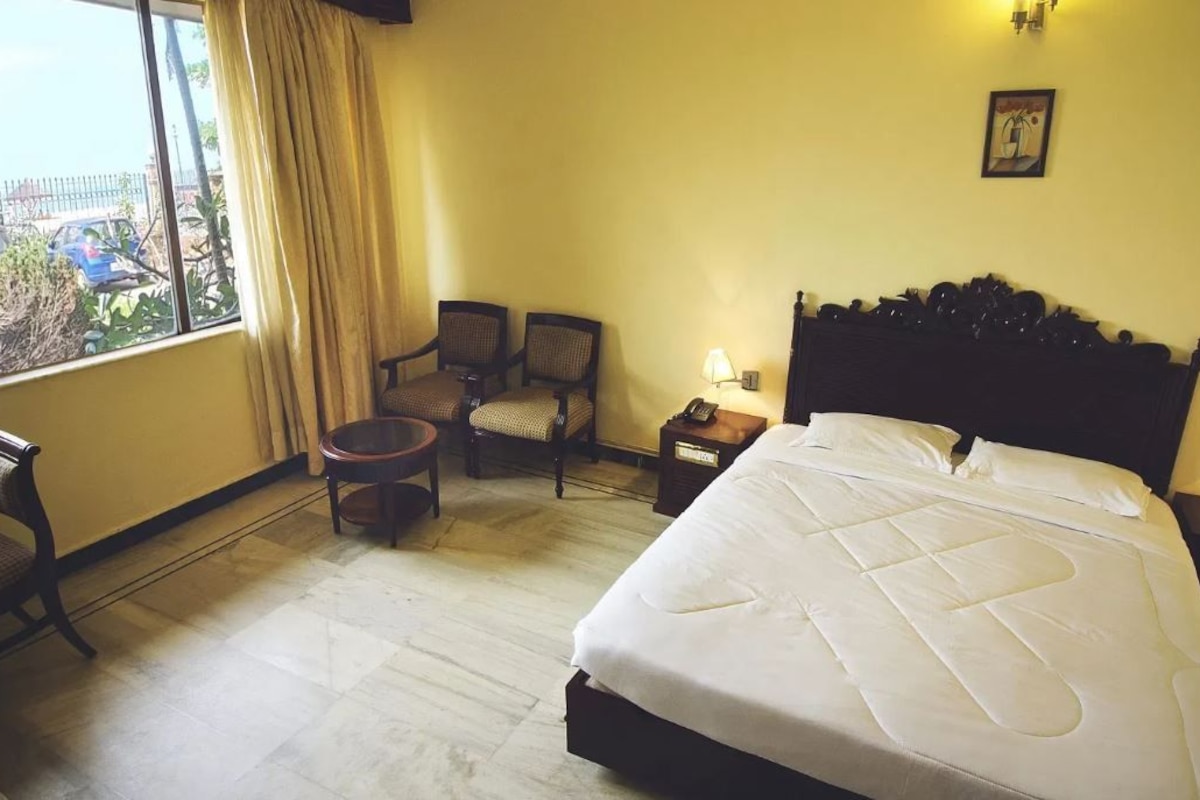 A hotel room with a large bed, two chairs, a small table, and a window with curtains.