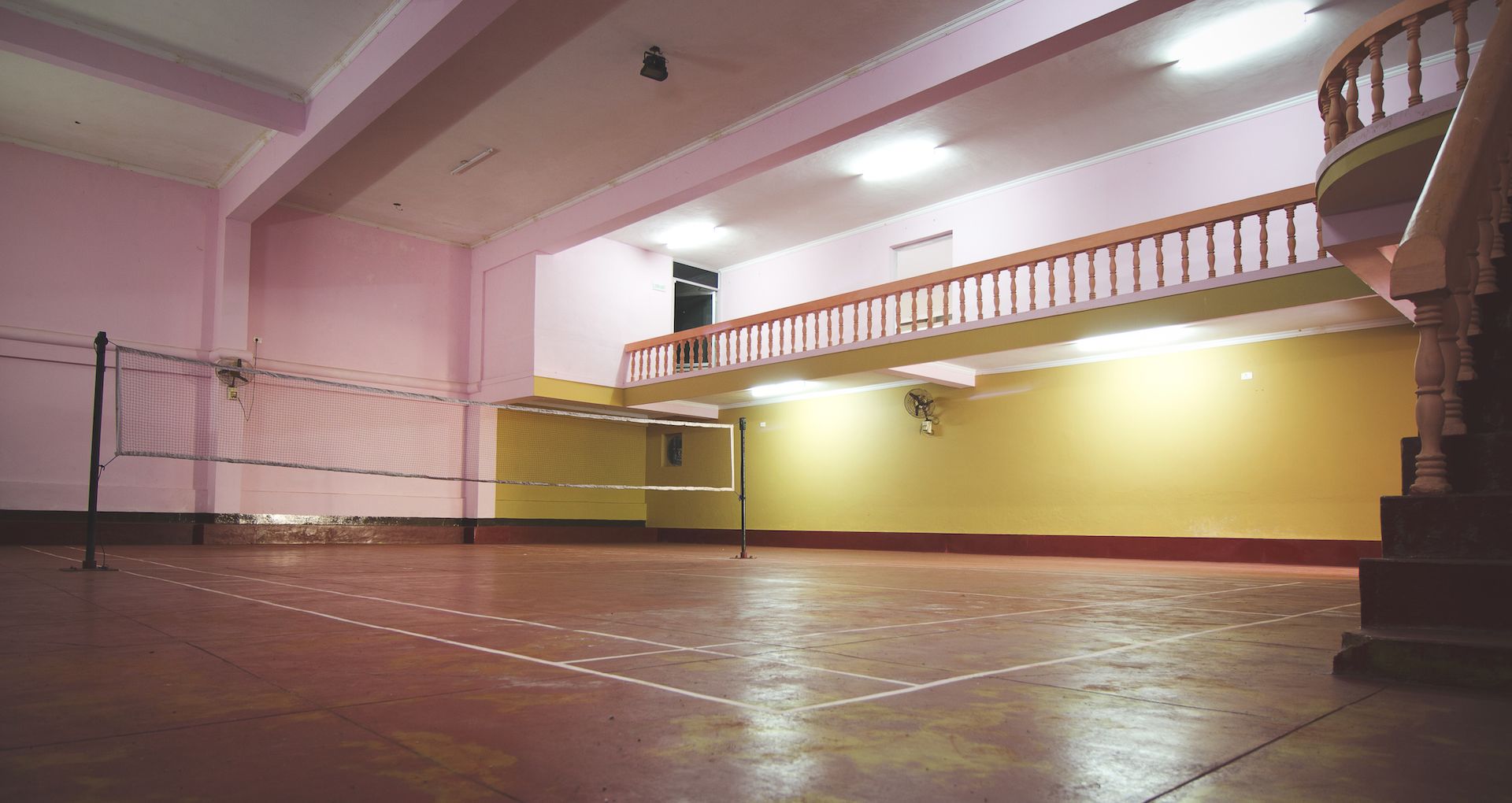 An indoor badminton court with a net, a staircase, and a balcony.