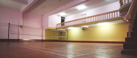 An indoor badminton court with a net, a staircase, and a balcony.