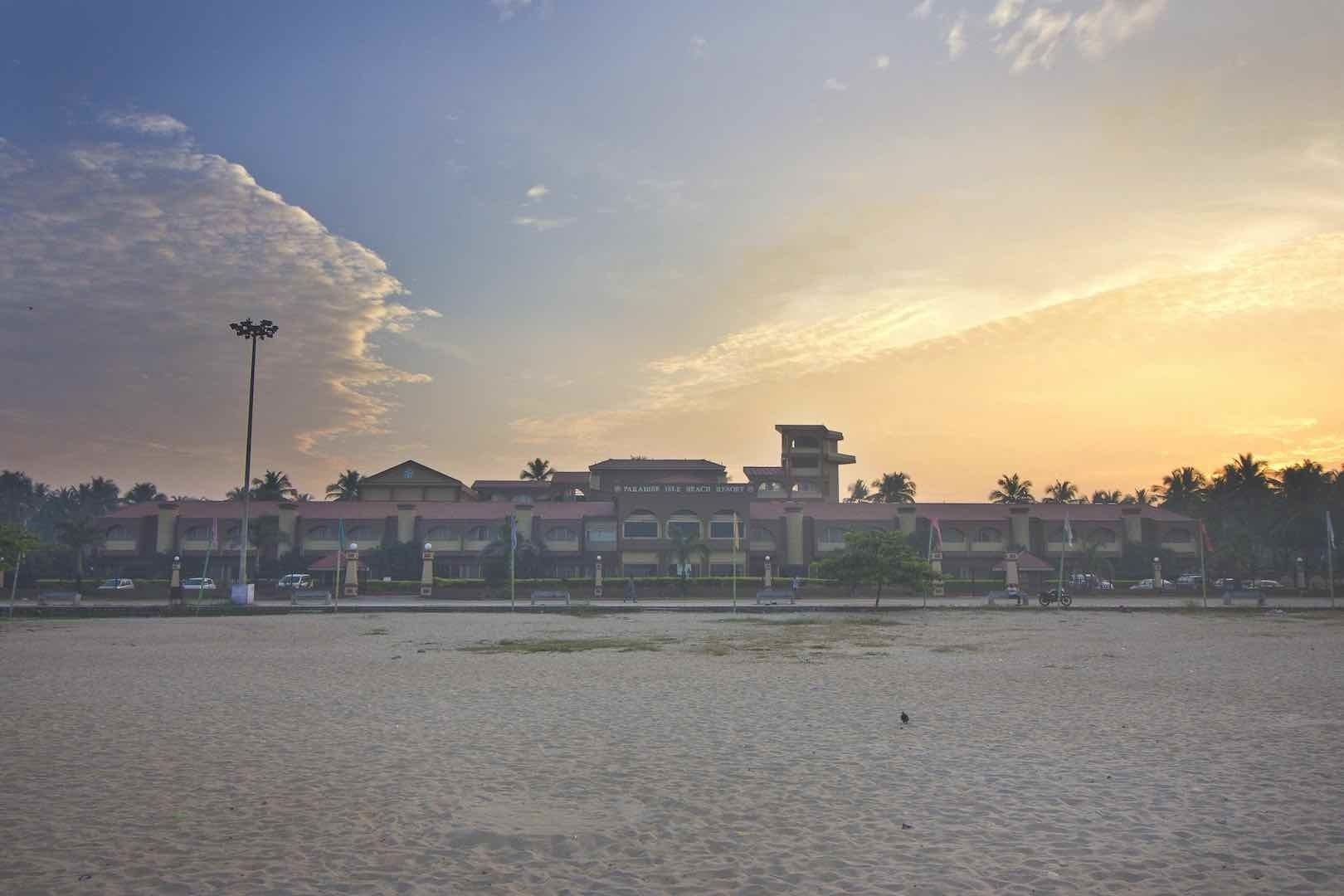 Un hôtel en bord de mer composé de plusieurs bâtiments, doté d’une tour imposante, et offrant une plage de sable en premier plan.