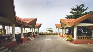 A covered outdoor seating area with multiple tables and chairs, columns, and a view of the sea. - Paradise Isle Beach Resort (Udupi)