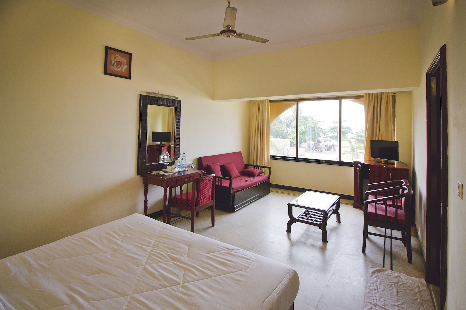A hotel room with a bed, a desk, a chair, a sofa, a TV, and a window with curtains.