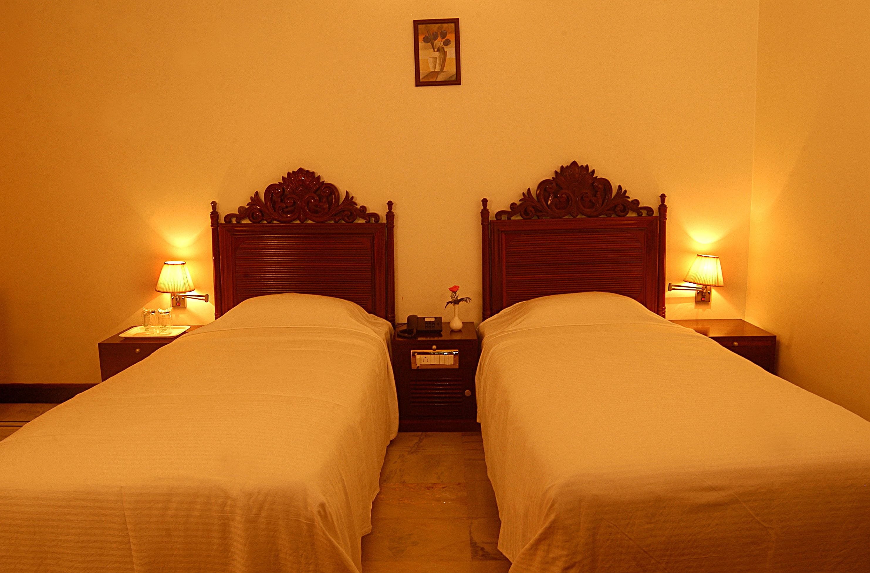 A hotel room with two single beds, nightstands with lamps, a small table with a vase, and a framed picture on the wall.