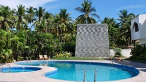 A pool area with two circular pools, surrounded by palm trees and a modern building with a zigzag pattern facade. - Paradise Isle Beach Resort (Udupi)