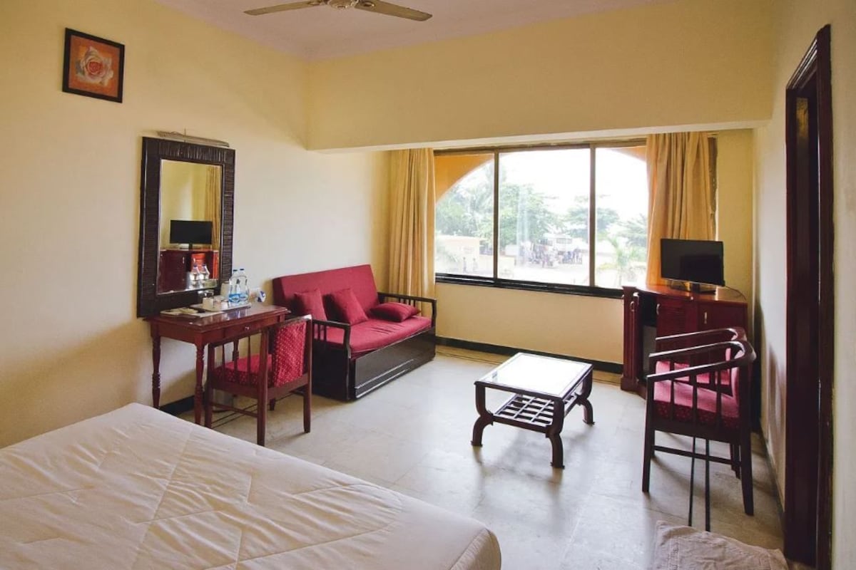 A hotel room with a bed, a desk, a red sofa, a TV, and a window with curtains.