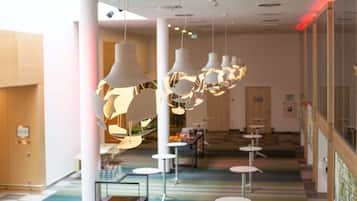 En moderne hotellobby med hængende pendellamper, en central trappe og et siddeområde med runde borde.