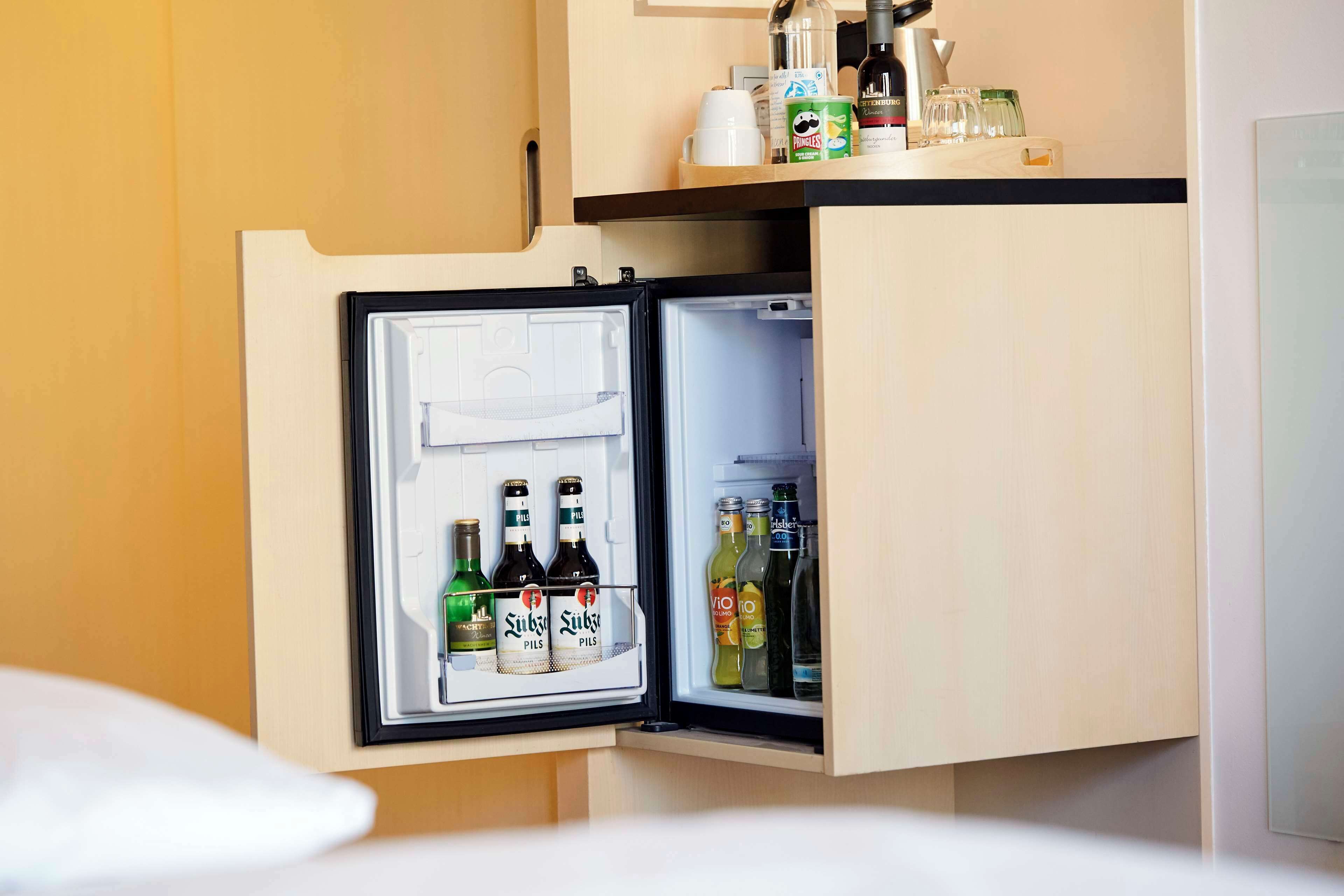 A hotel minibar with a refrigerator containing beverages and a bottle of water.