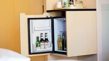 A hotel minibar with a refrigerator containing beverages and a bottle of water.
