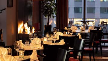 A restaurant with tables set for dining, a fire feature, and a view of buildings outside.