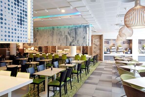 A modern dining area with multiple tables and chairs, a patterned wall, and a bar area in the background. - Scandic Berlin Potsdamer Platz (Berlin)