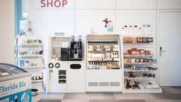 Una tienda con estantes llenos de aperitivos y bebidas, una máquina de café y una vitrina con juguetes.