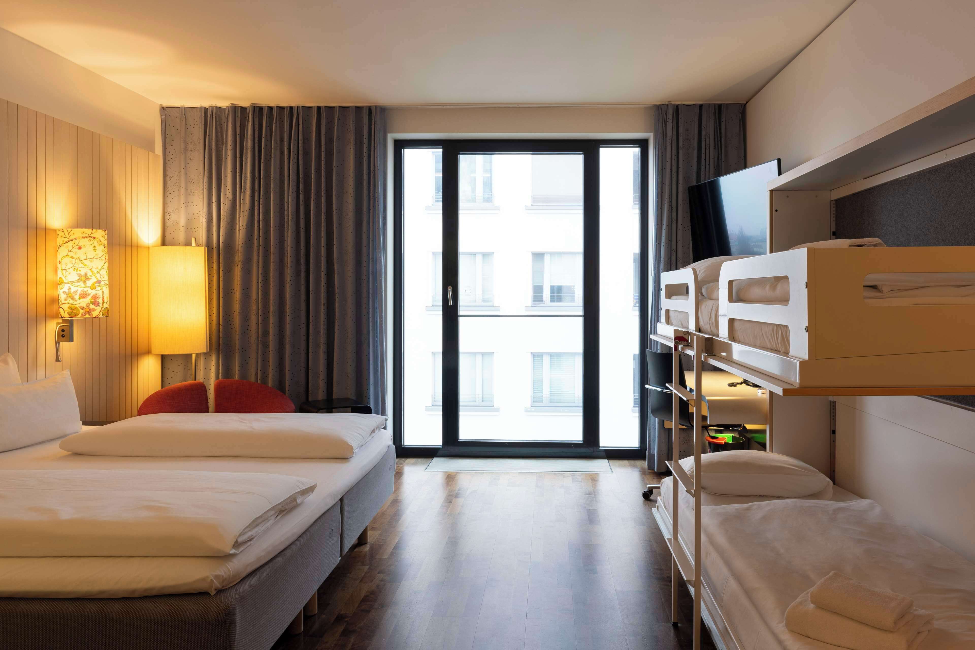 Ein Hotelzimmer mit zwei Betten, einem Fernseher und einem großen Fenster mit Vorhängen.