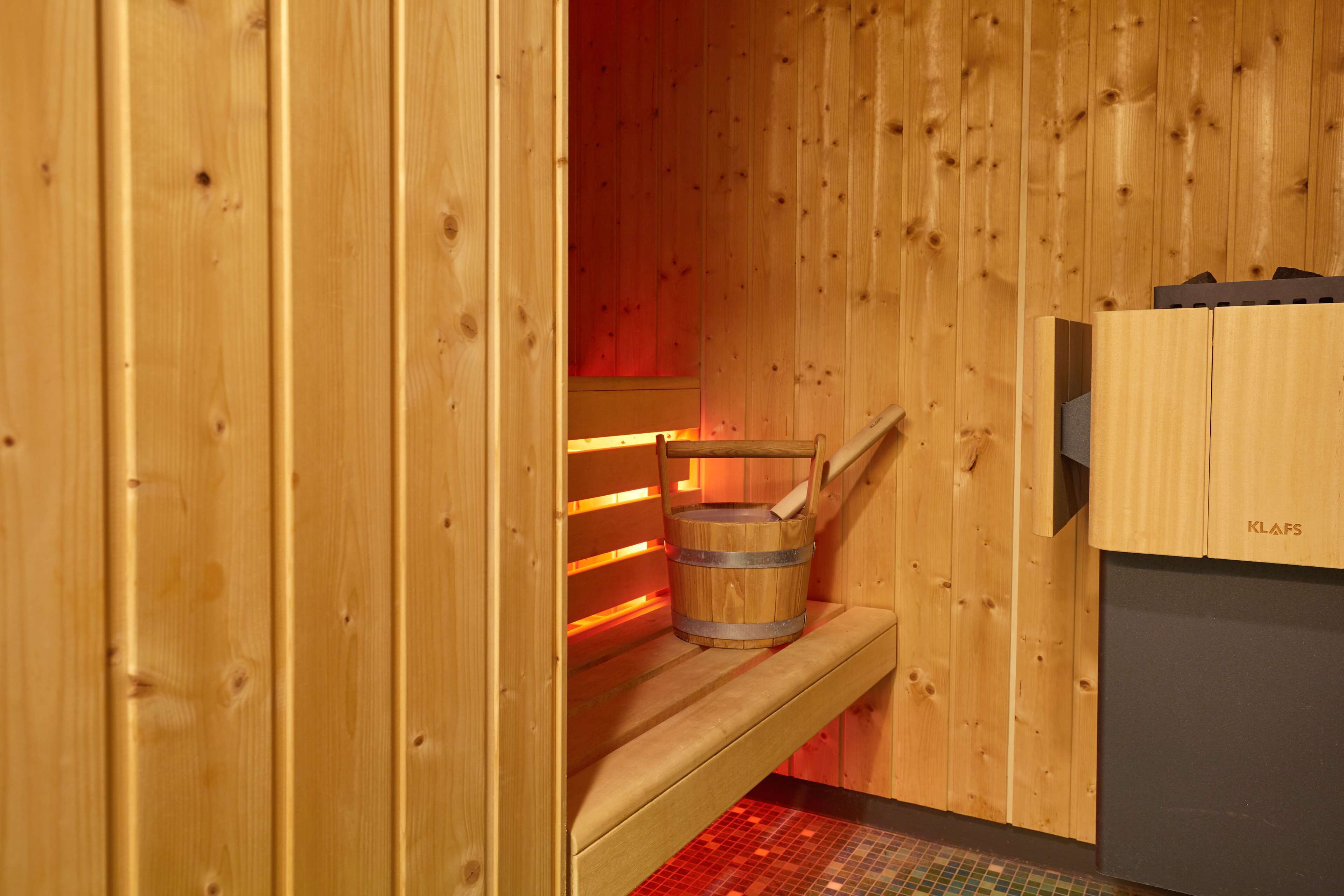 Een houten sauna met een bank, een emmer en een sauna-kachel.