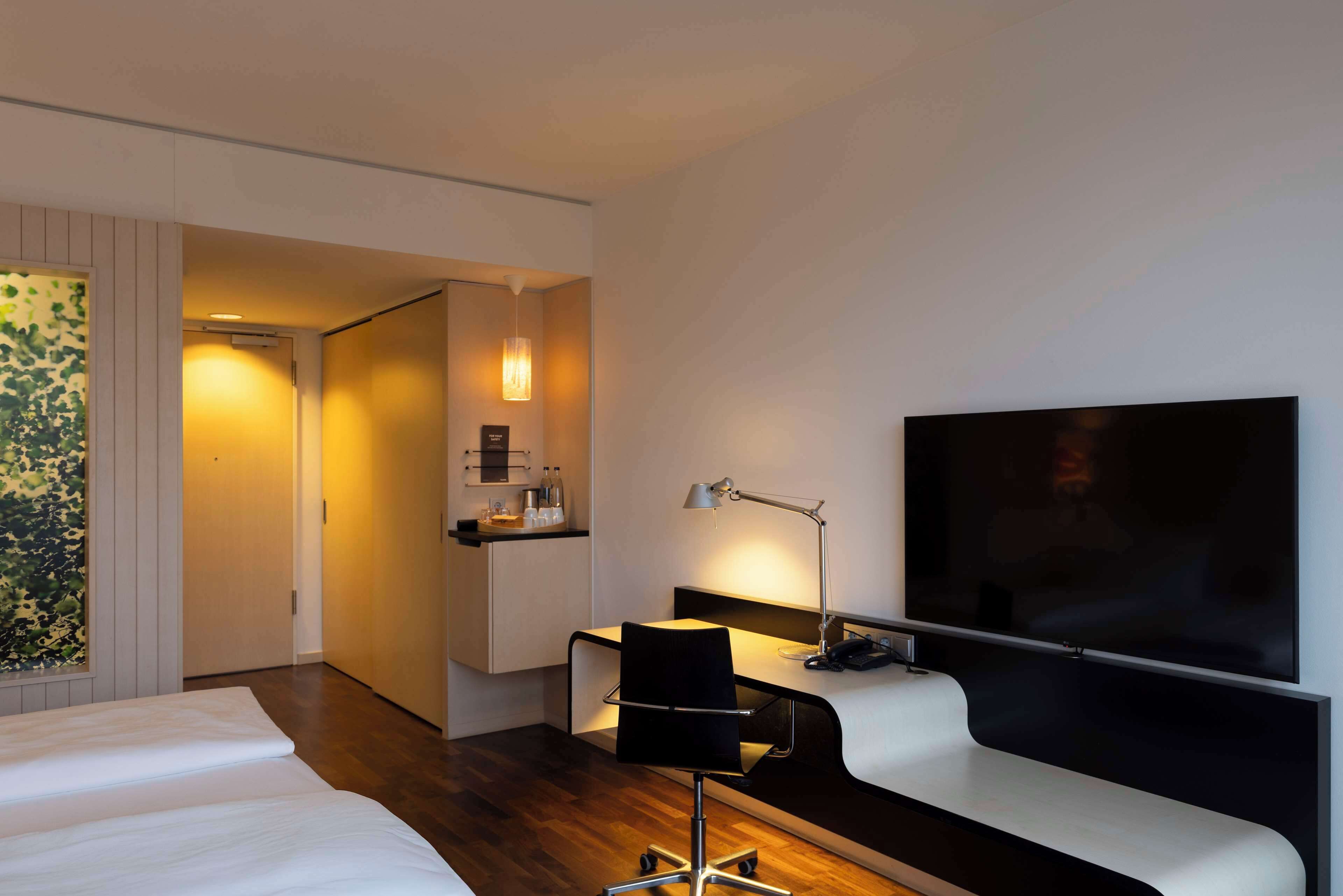 Ett modernt hotellrum med en säng, ett skrivbord med en stol, en platt-TV och en TV som är monterad på väggen.