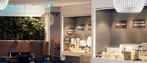 A café with tables and chairs, a counter with food items, and a wall with a sign.