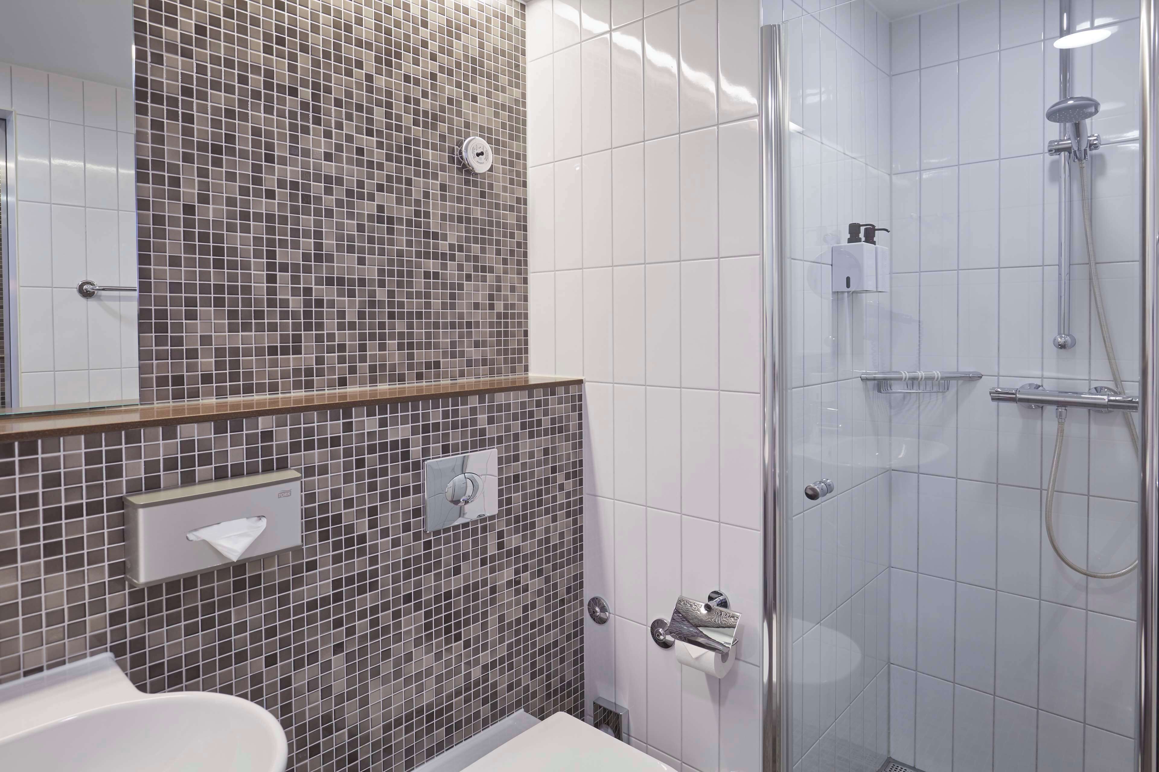 Kylpyhuone, jossa on laatoitettu suihku, peili, wc ja pesuallas.
