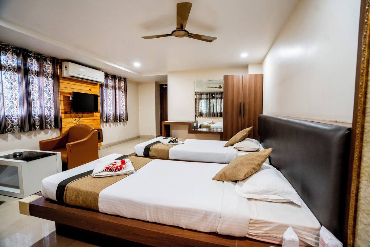 A hotel room with two beds, a desk, a chair, a ceiling fan, and a mirror.