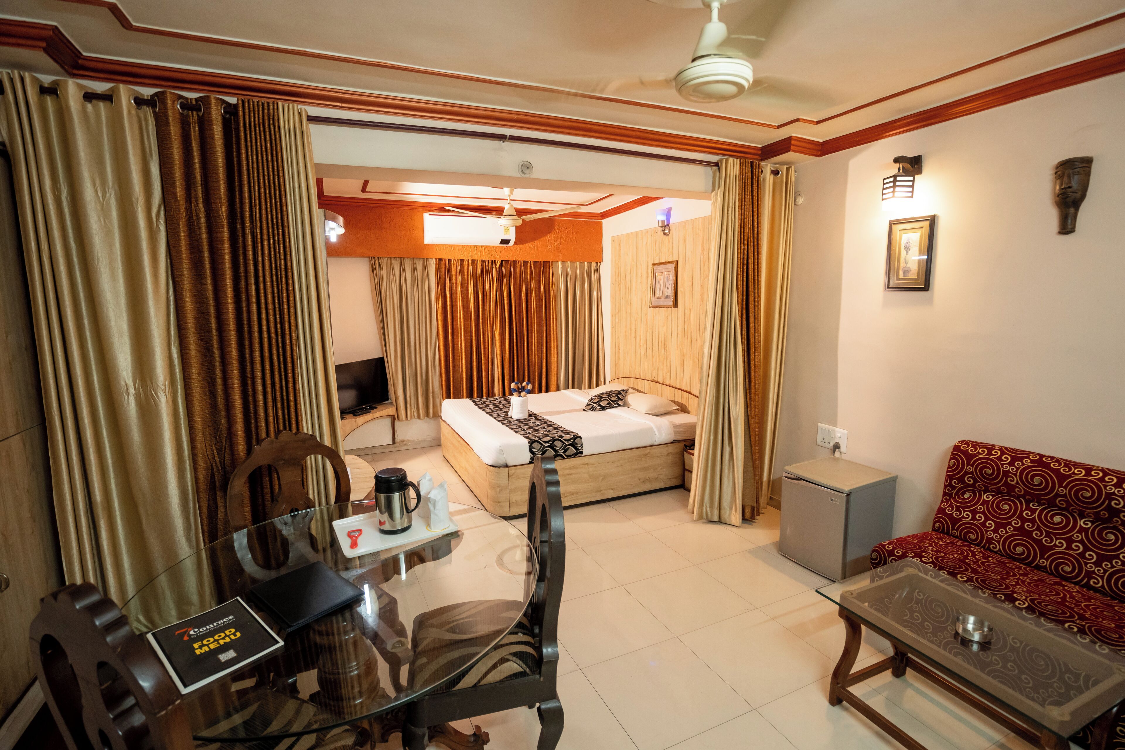 Una habitación de hotel con cama, sofá, mesa de centro, escritorio con computadora y un refrigerador pequeño.