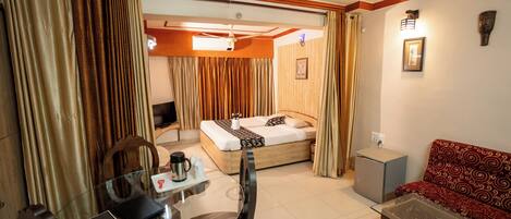Una habitación de hotel con cama, sofá, mesa de centro, escritorio con computadora y un refrigerador pequeño.