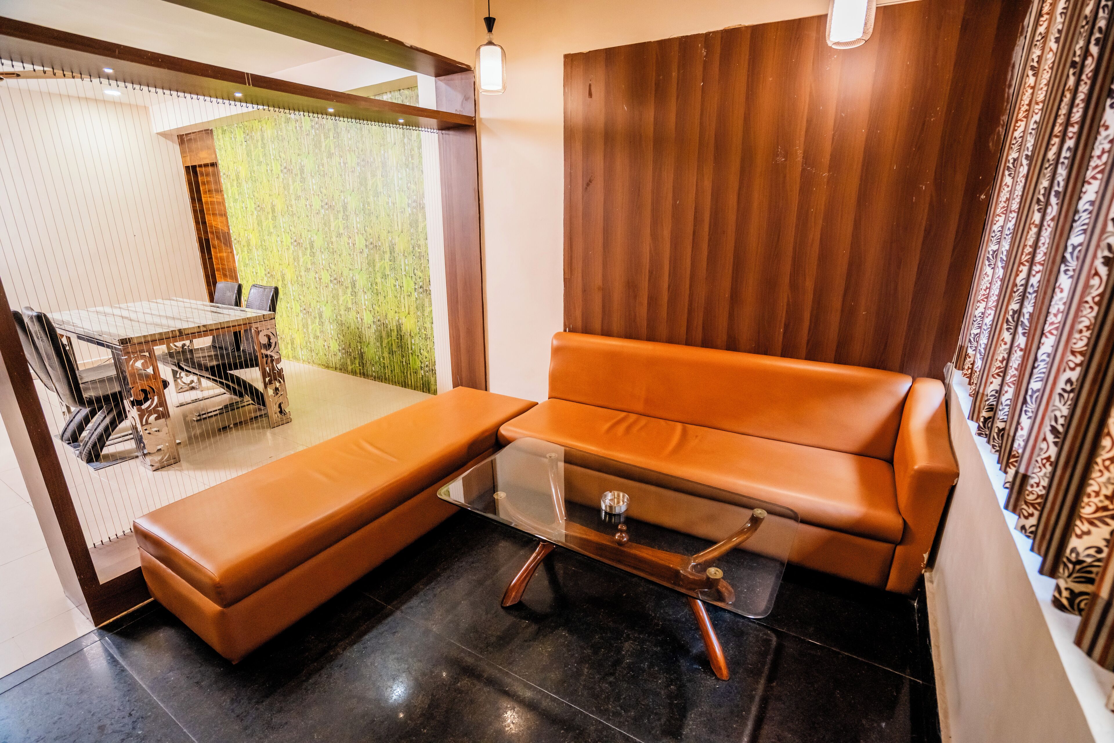 A modern living room with a brown leather sofa, a glass coffee table, and a dining area with a table and chairs.