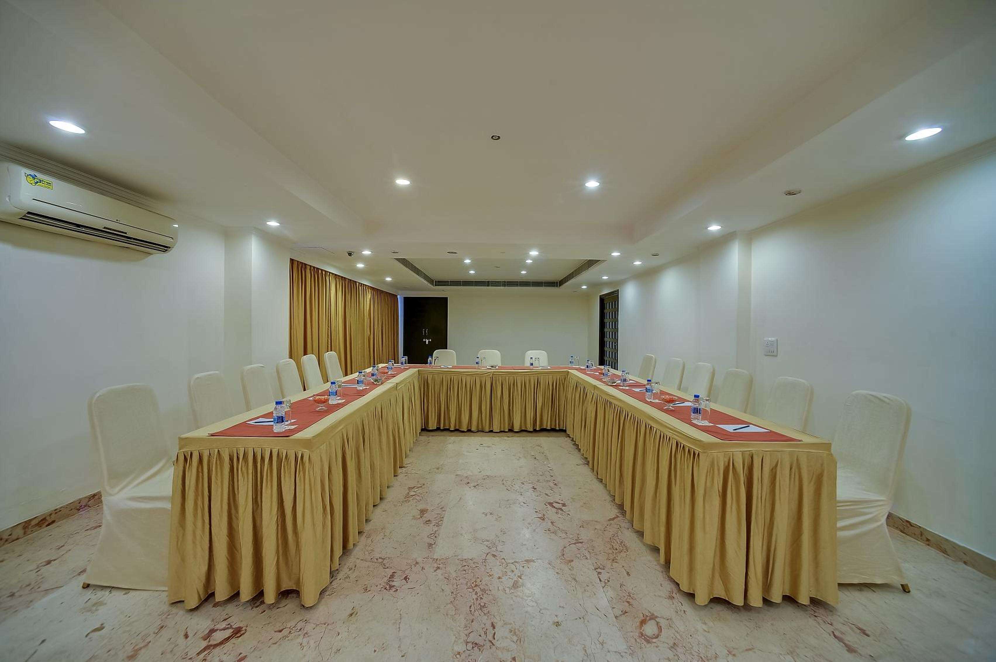 Un salón de conferencias con una larga mesa, sillas blancas y un aire acondicionado instalado en el techo.